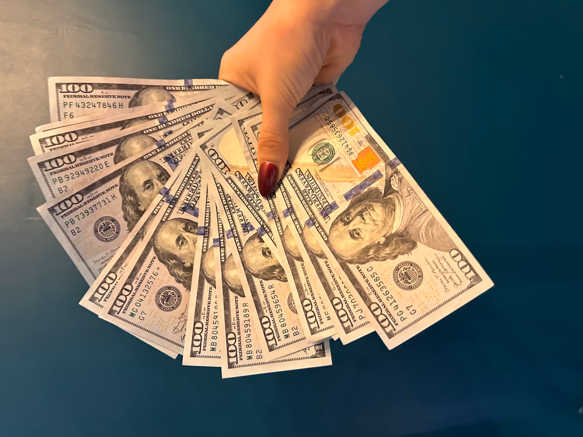 Princess Rose holding a fanned-out spread of hundred dollar bills — financial domination tribute